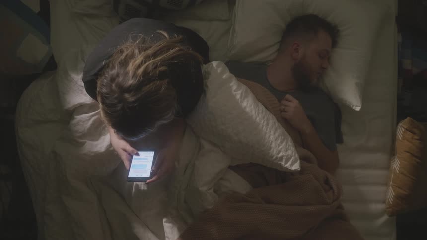 A woman sits up in bed texting