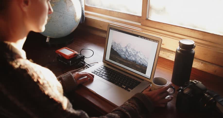 A woman uses a laptop and takes a drink