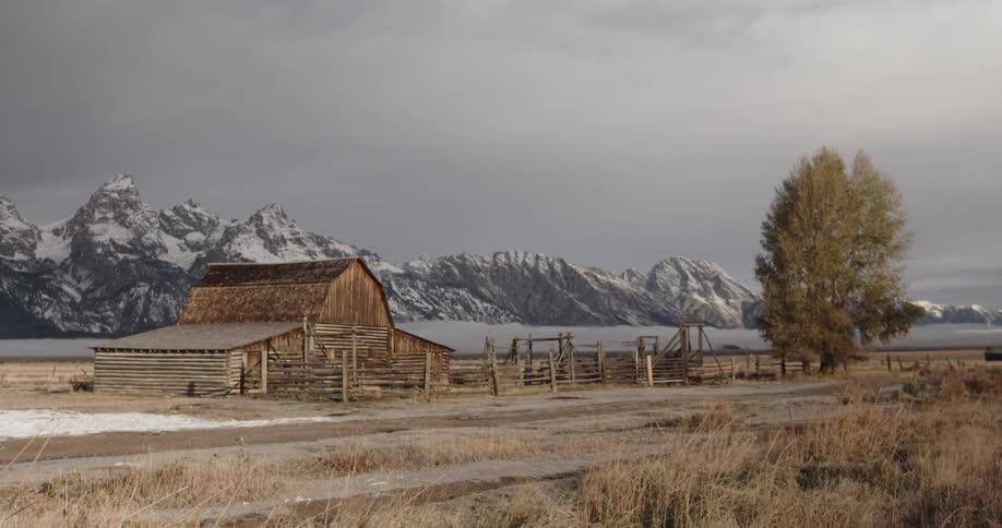 A barn is shown with snowy mountains in the distance