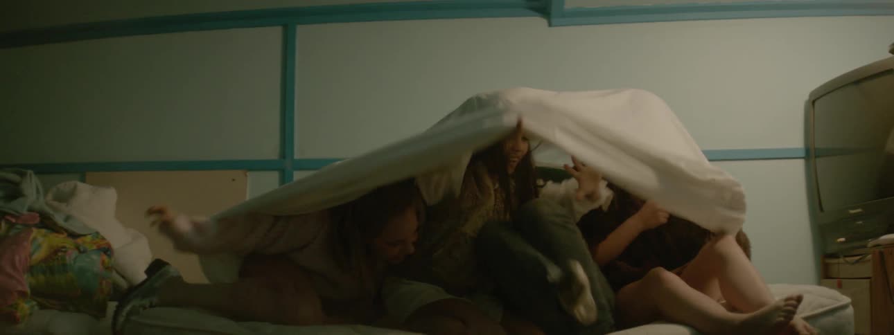 Three girls play under a sheet on a bed