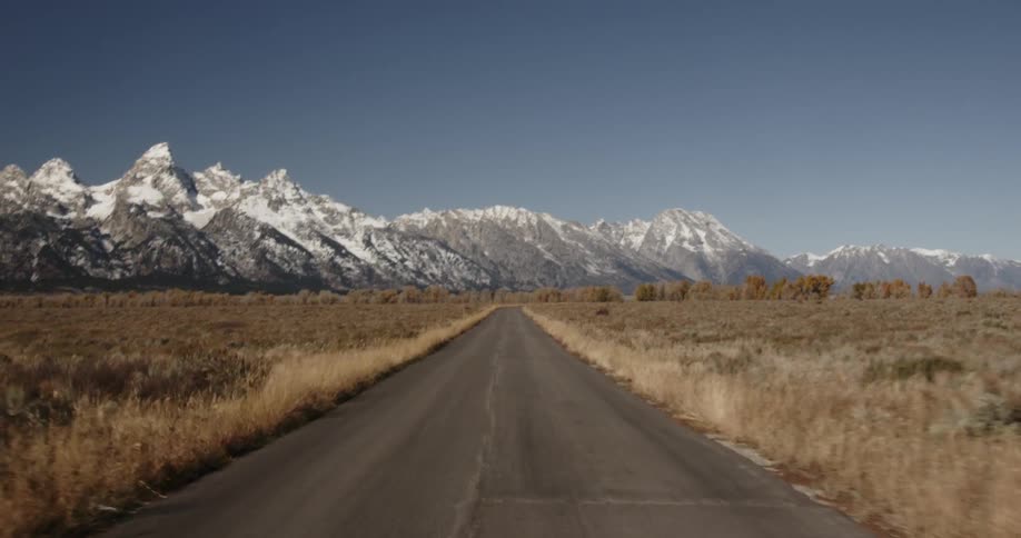 A road leading to jagged snow-capped mountains