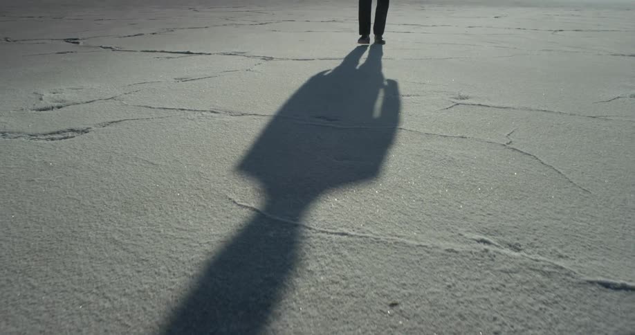 A man walks across salt flats while casting his shadow on the ground
