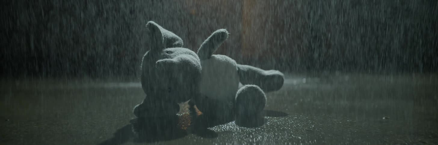 A stuffed elephant lays on the sidewalk in the rain
