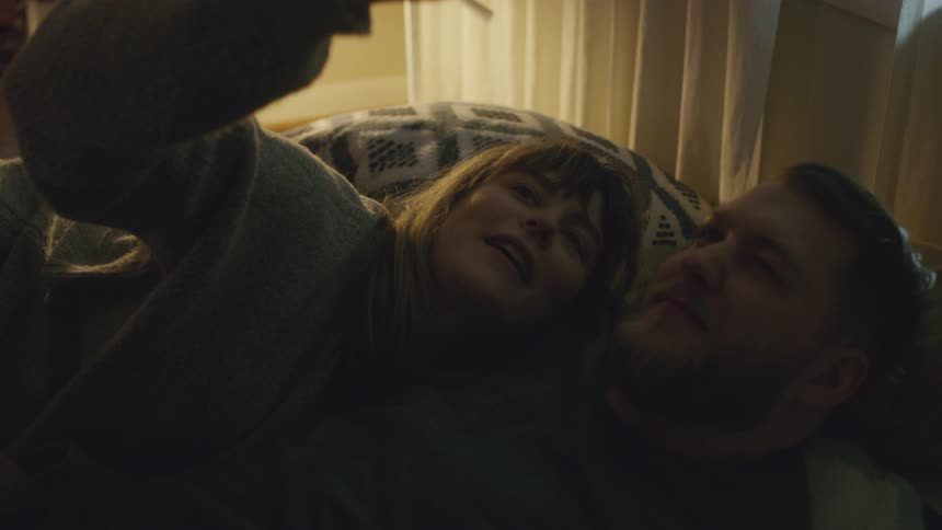 A man and woman take a selfie while laying in bed