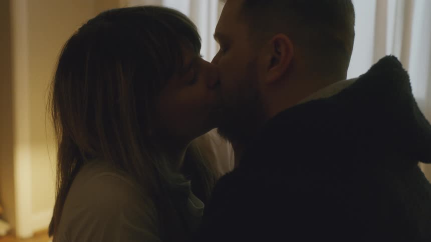 A man and woman kiss while sitting in bed