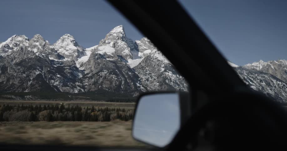 Snowy mountains are seen through a car's window