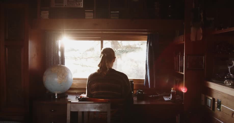 A woman sits at a desk with sunlight streaming in the window