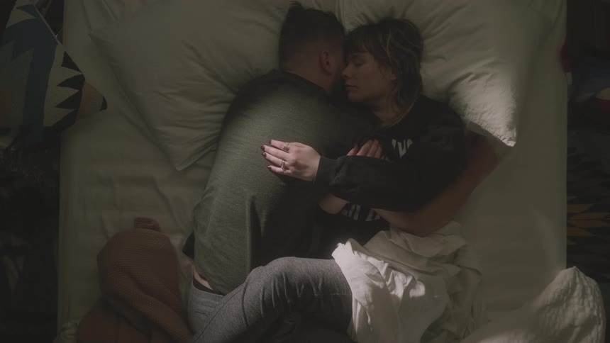 A man and woman snuggle close in bed