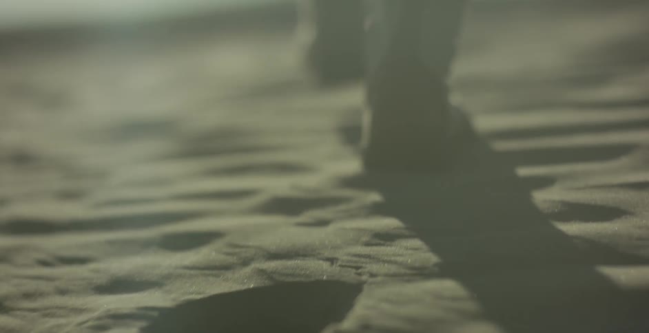 A person in boots walks across fine sand