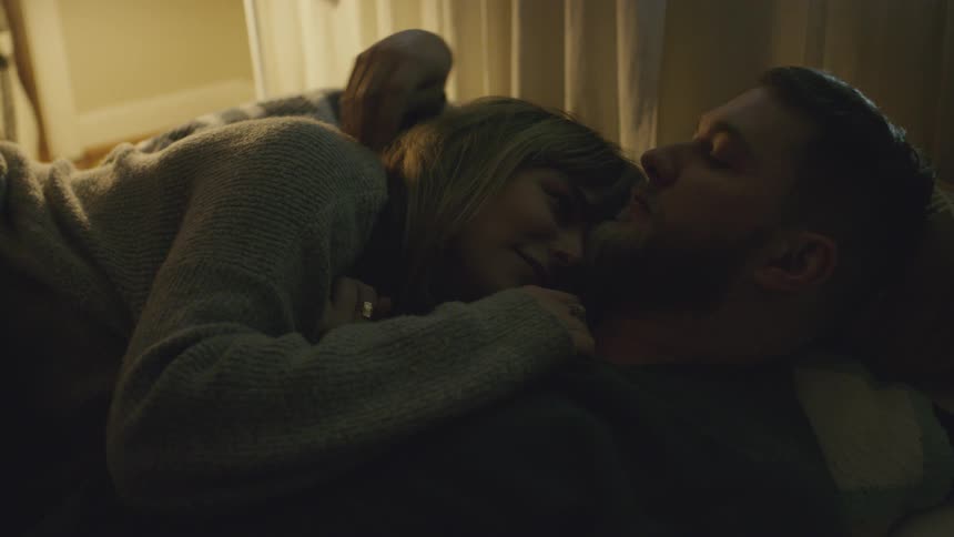 A woman lays her head on a man's chest in bed