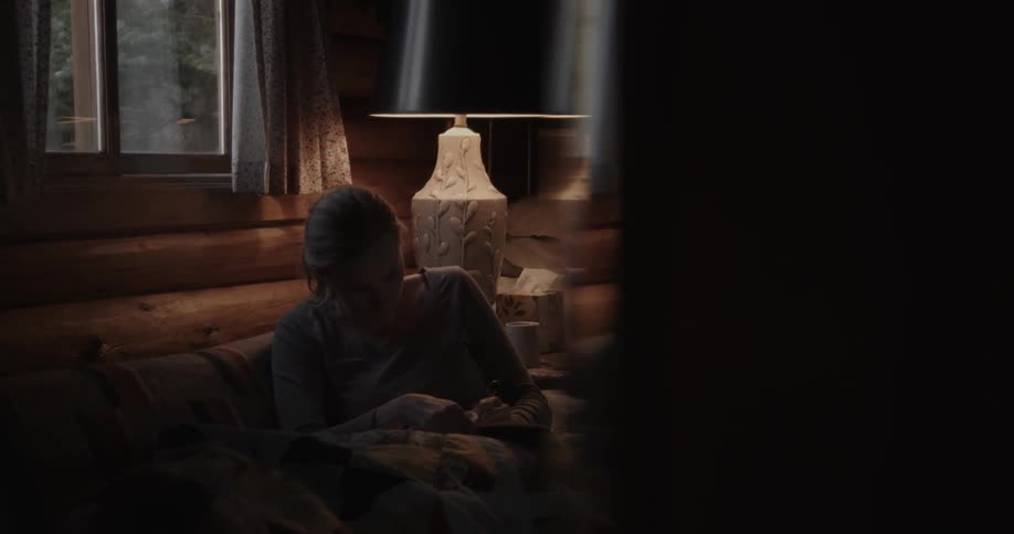 A woman reads a bible while wrapped in a blanket on the couch