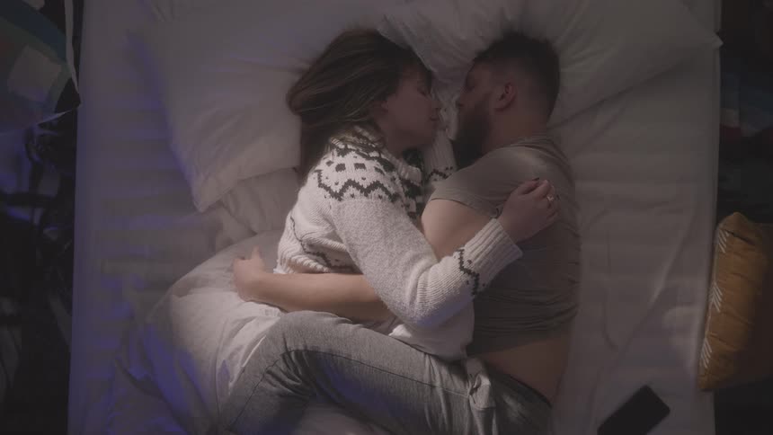 A man and woman embrace while in bed