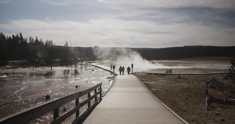 People walk across a bridge over steaming water