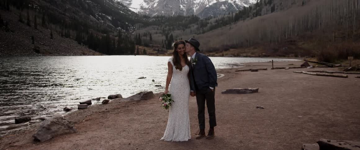 Man wearing a suit kisses woman wearing a dress next to water
