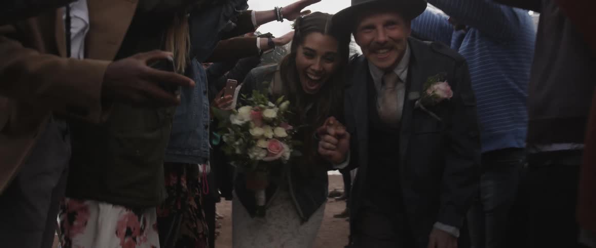 A bride and groom hold hands while walking beneath outstretched hands