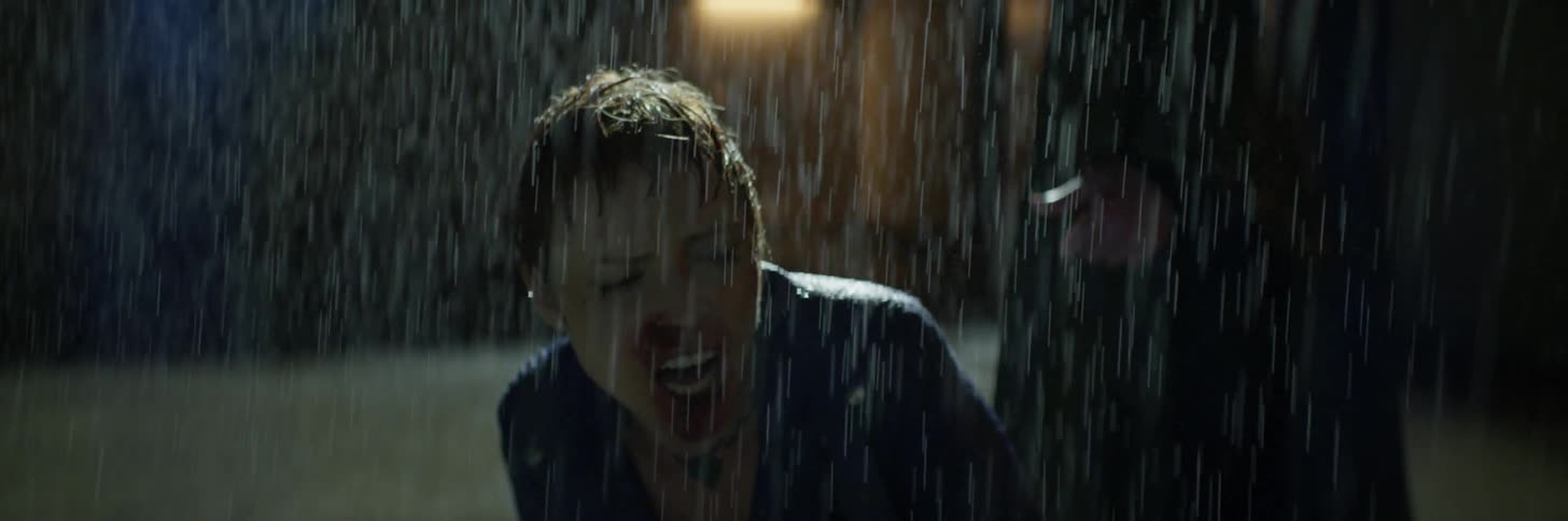 A bleeding woman screams while a man circles her in the rain