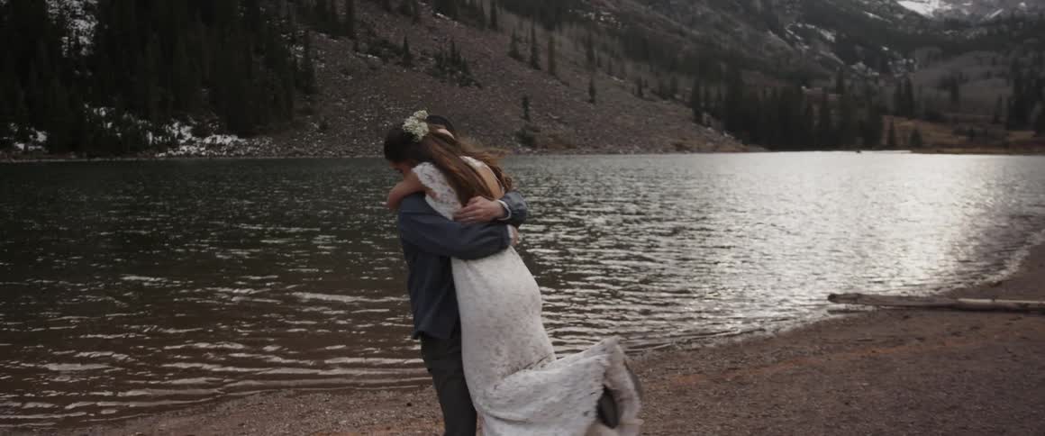 Bride and groom hug and twirl around next to water
