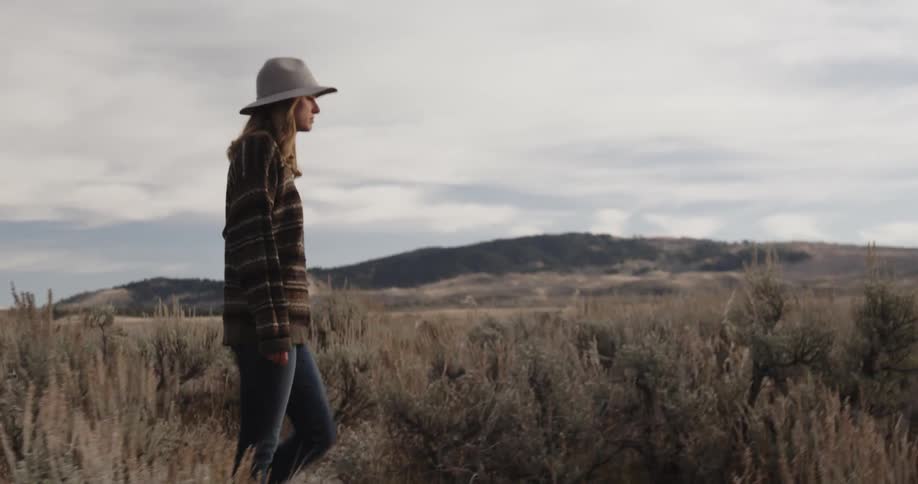 A woman walks through a field on a cloudy day