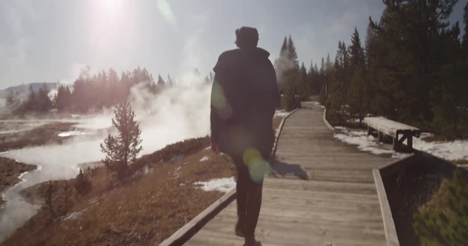 Person walking down a wooden sidewalk next to a steaming river