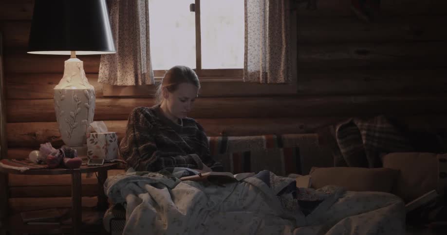 A woman sits on a couch with a blanket and reads a book