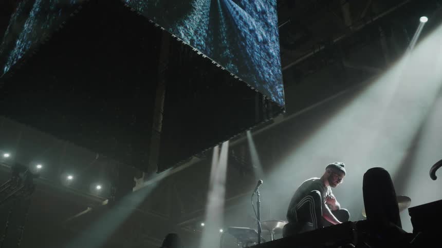 A man crouches on a stage with lights shining down