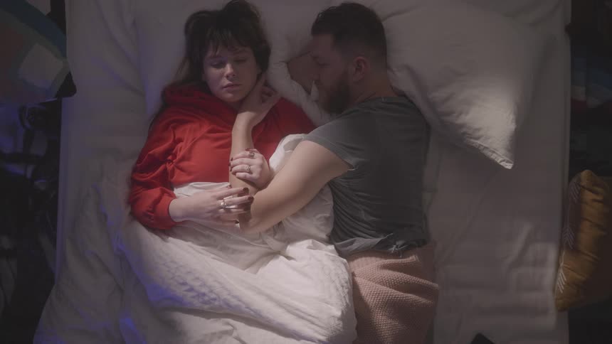 A man touches a woman's face in bed