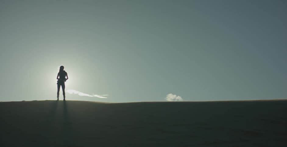 A woman stands atop a hill in sunlight