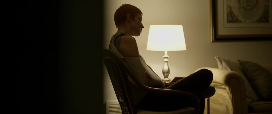 A red haired woman sits cross-legged in a chair