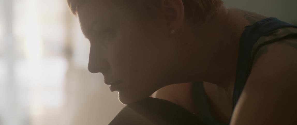A woman rests her chin on her knee as sunlight pours in the window