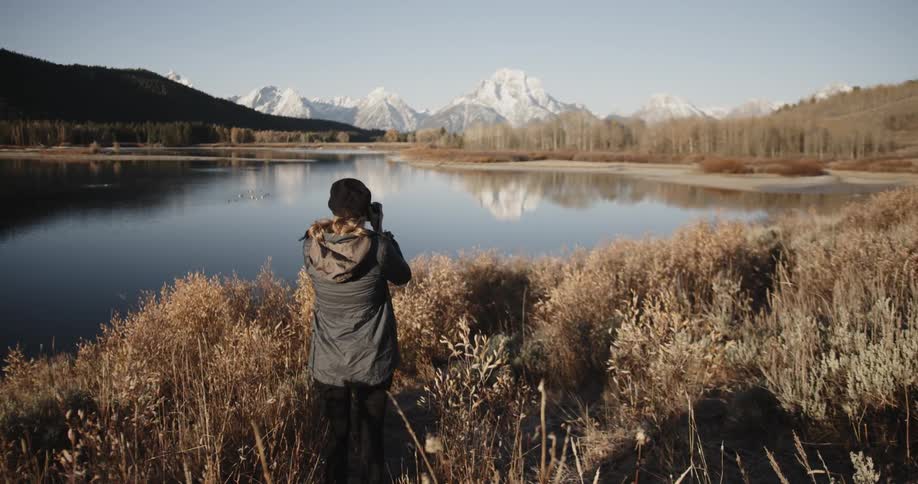 A woman takes a photograph of a mountain lake