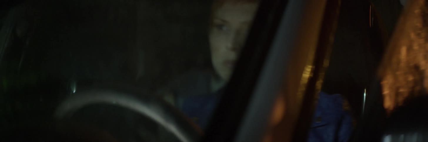 A woman exits a car while it rains at night