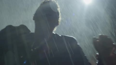Two people fight each other in the rain at night