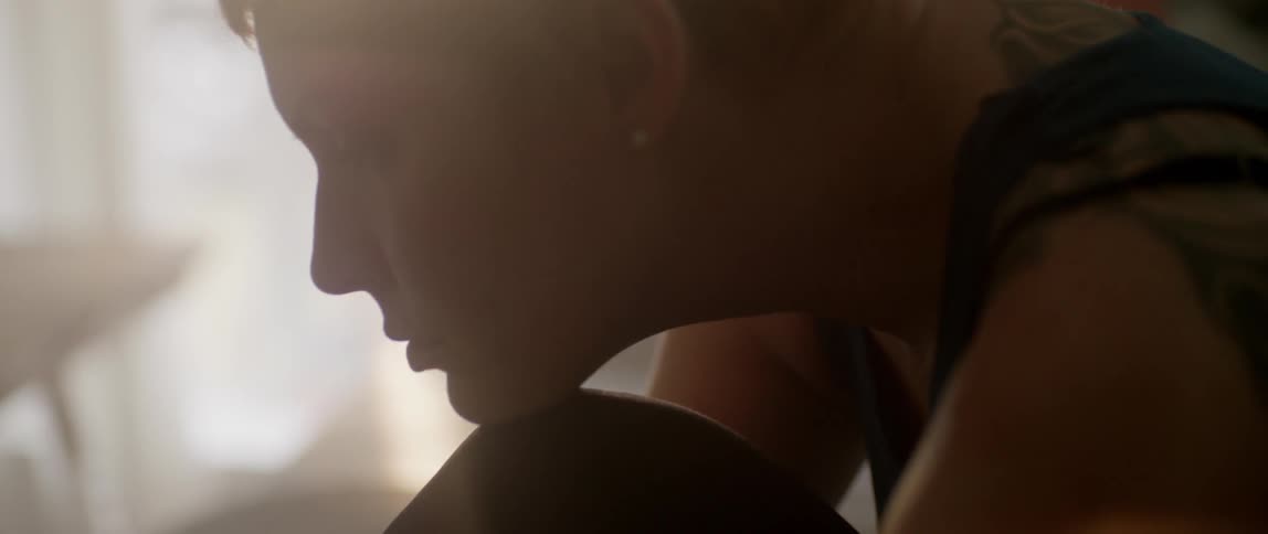 A woman rests her chin on her knee with sunlight pouring in the window