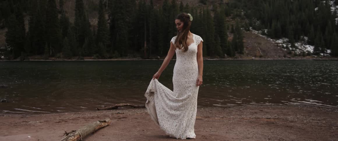 A bride stands on a mountain lakeshore