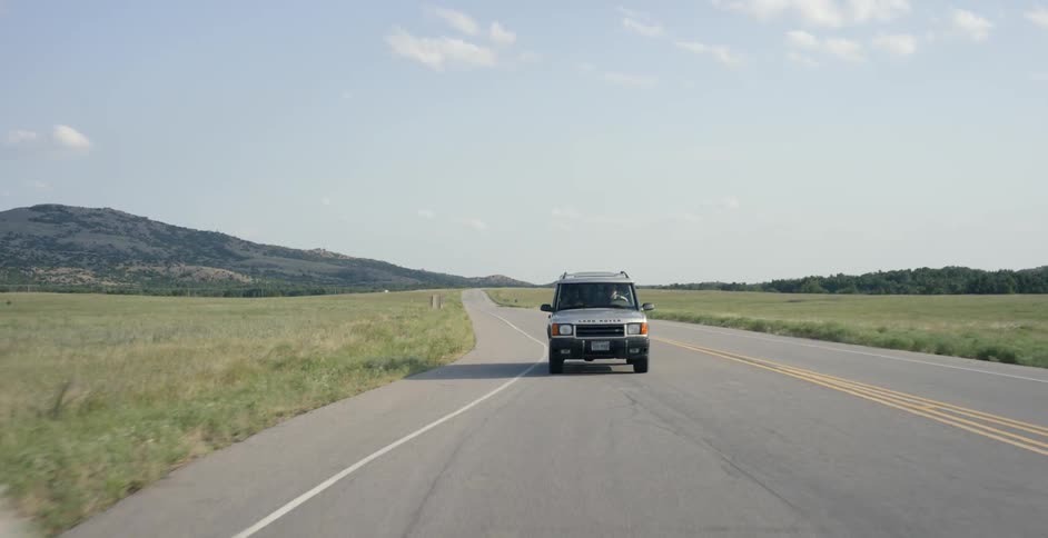 A car drives on a rural road on a sunny day