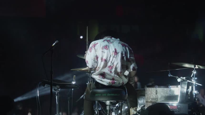 A man in a flowered shirt plays drums at a concert