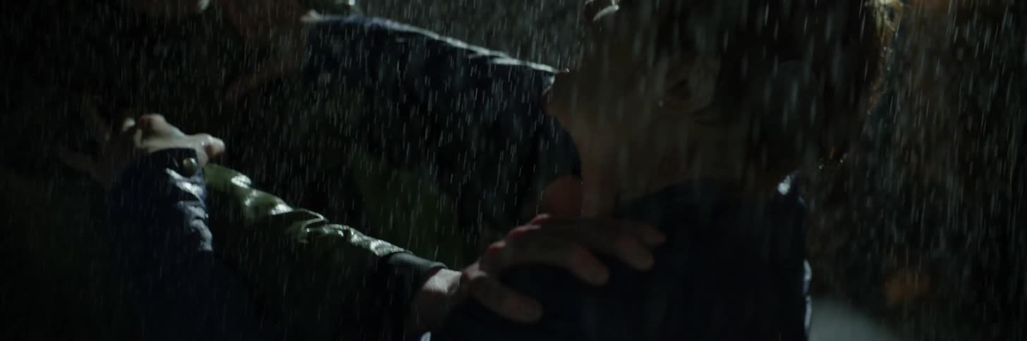 A man in a poncho holds back a red-haired person in the rain
