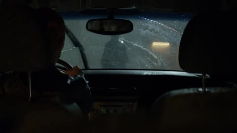 The driver of a car watches a person standing outside in the rain