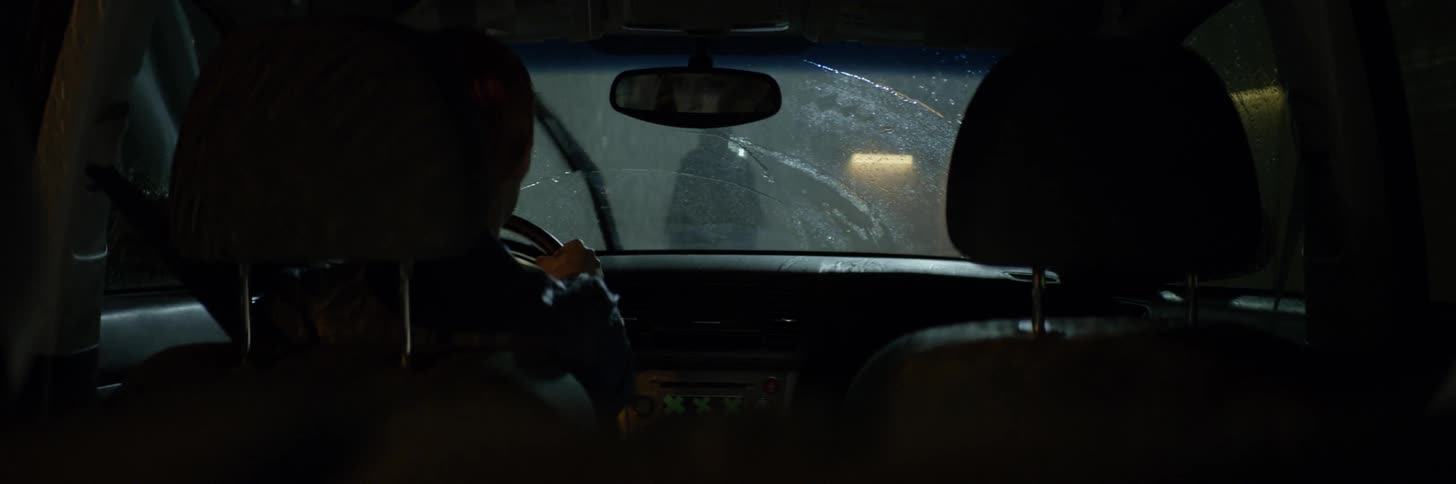 The driver of a car watches a person standing outside in the rain