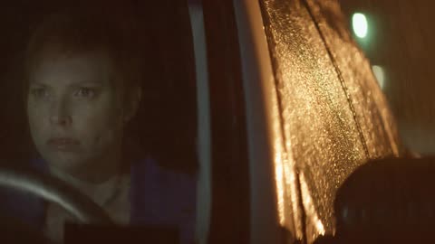 A woman sits in a car while it rains outside