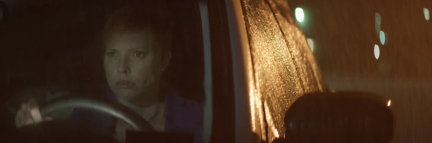 A woman sits in a car while it rains outside