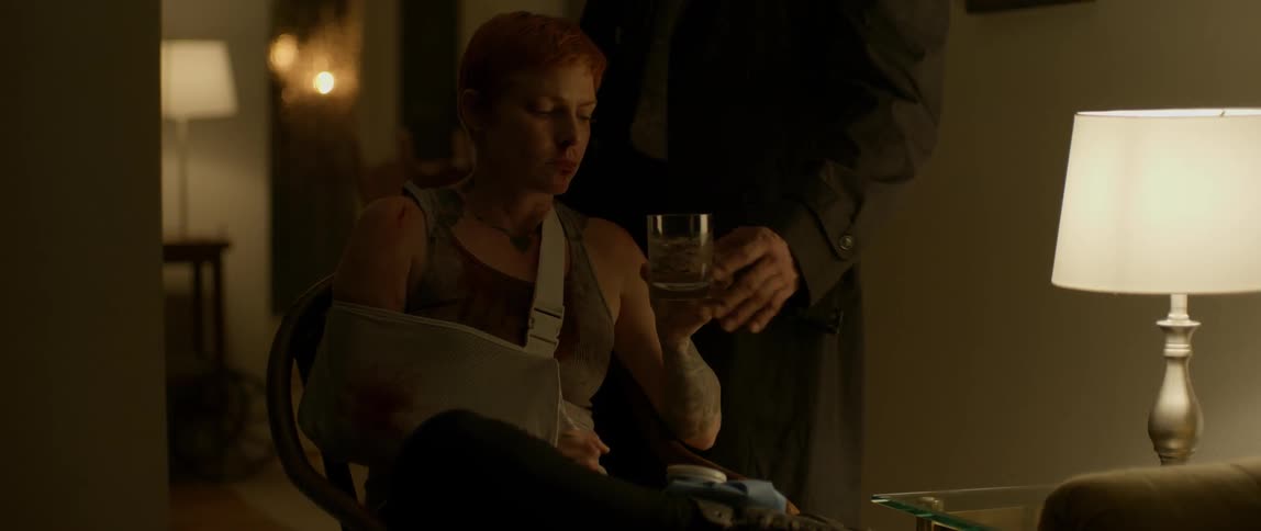 A bruised and bloody woman accepts a drink from a man in a coat