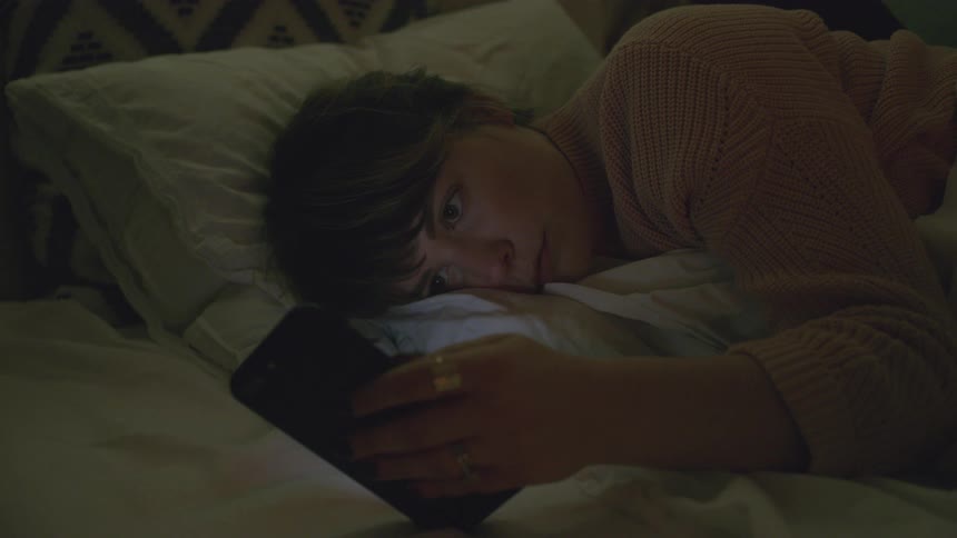 A woman looks at her phone in bed