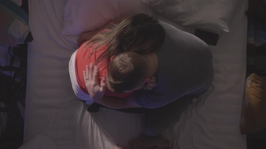 A man and woman kiss and hold each other on a bed