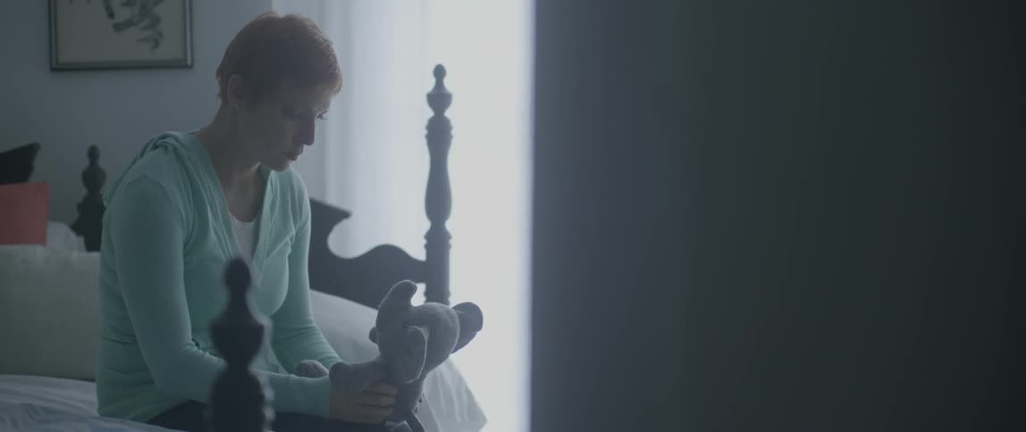 A woman sits on a bed while holding a stuffed elephant