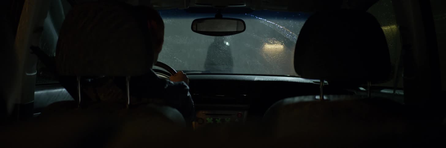 A woman sits in a car while watching a person in the rain outside