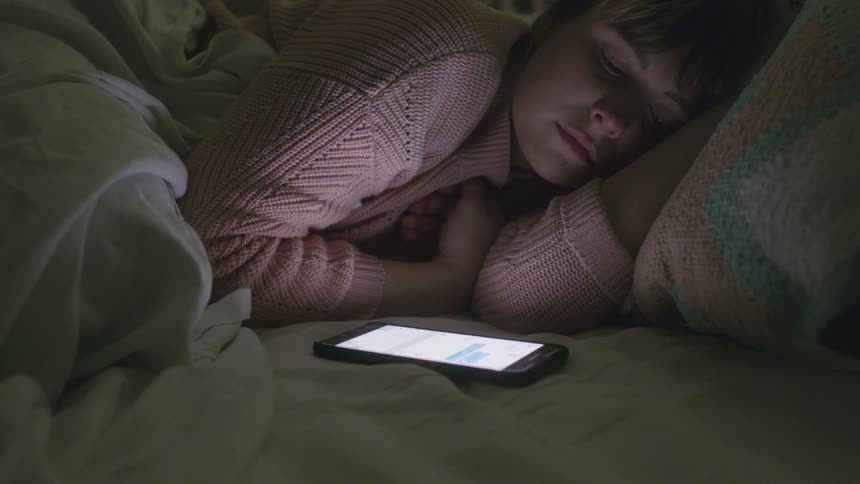 A woman watches her phone in bed
