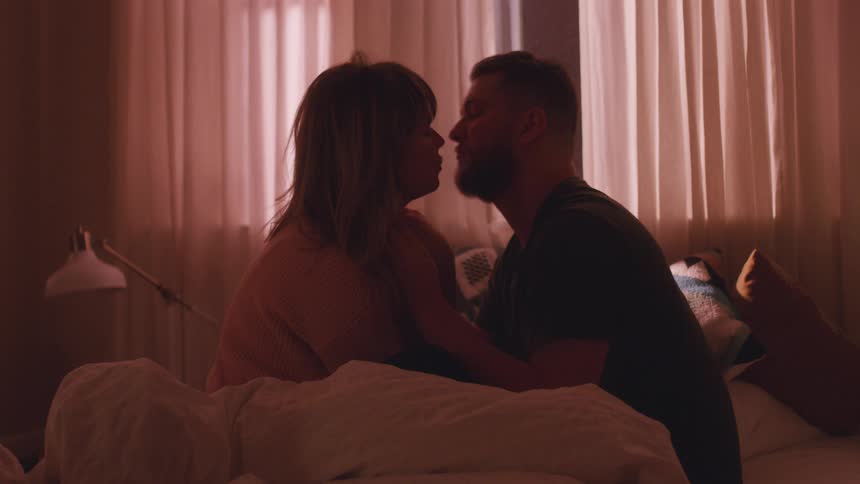 Man and woman sit on a bed kissing
