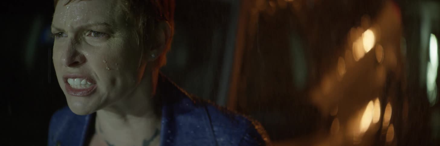 A woman stands beside her vehicle in the rain shouting and breathing heavy