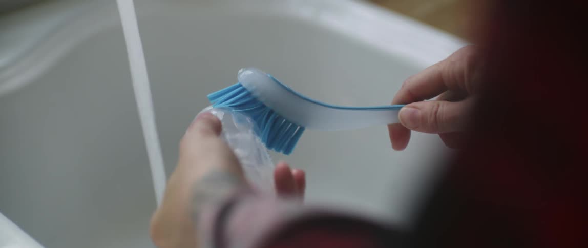 A person cleans a baby bottle with a scrub brush